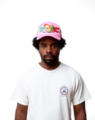 Person wearing a pink cap with colorful designs and a white t-shirt with a logo on a white background