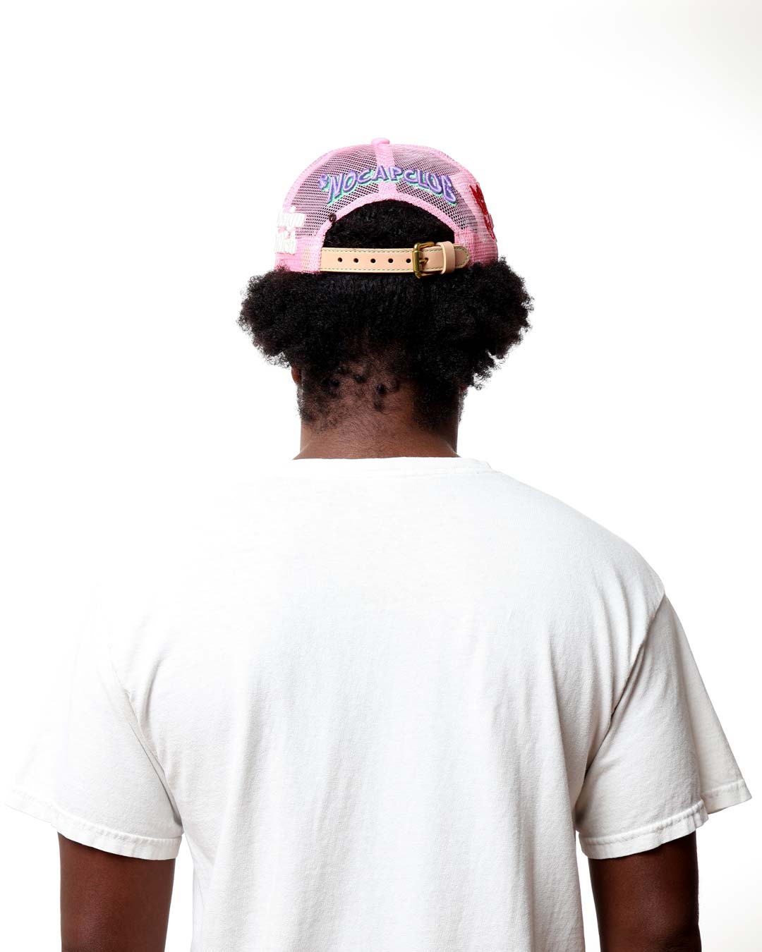 Person wearing a pink and black cap with text on the back, white t-shirt, and white background