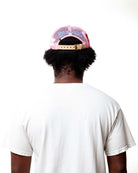 Person wearing a pink and black cap with text on the back, white t-shirt, and white background