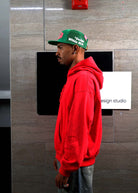 Man in red hoodie and green cap, side profile.