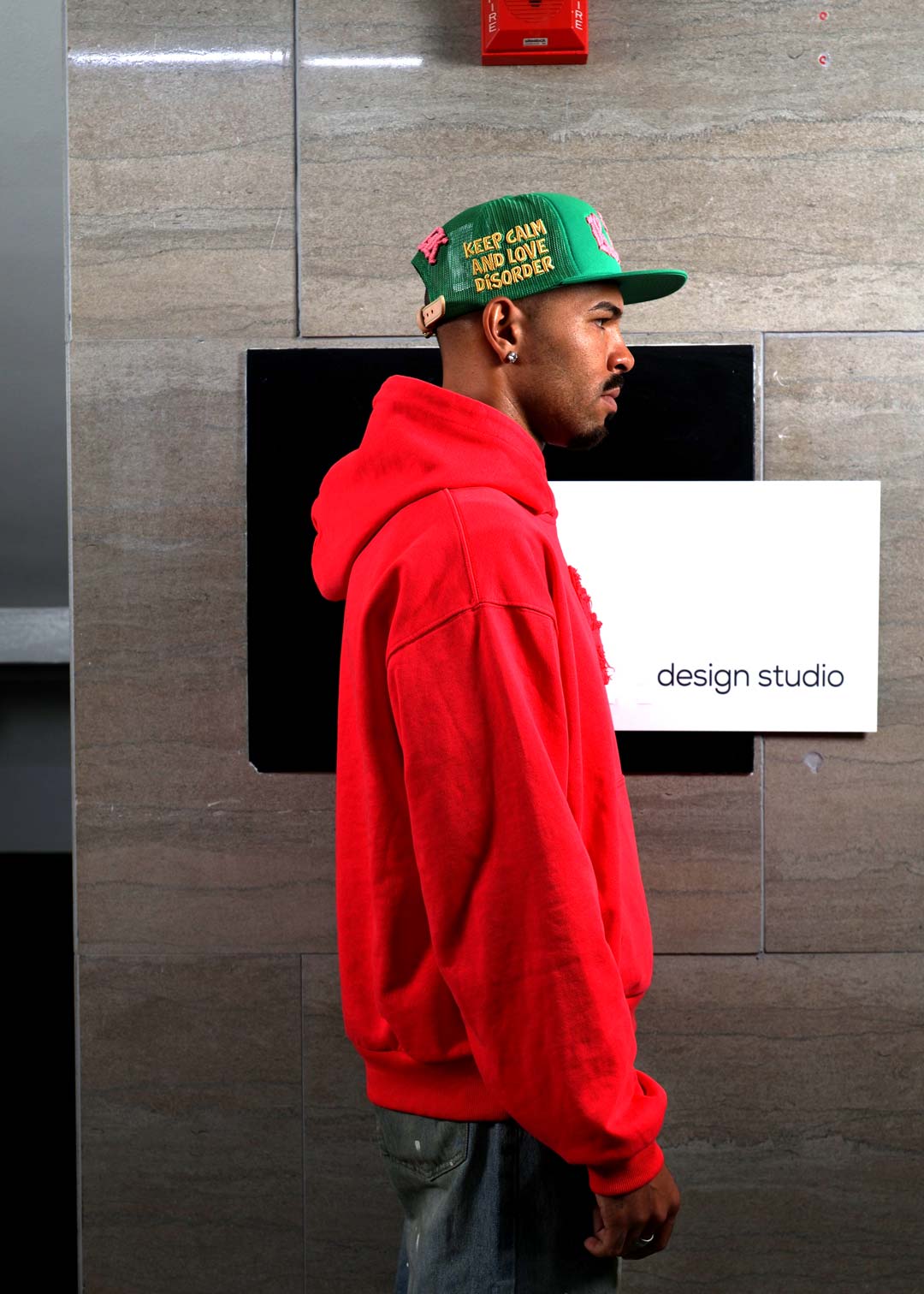 Man in red hoodie and cap, side profile.