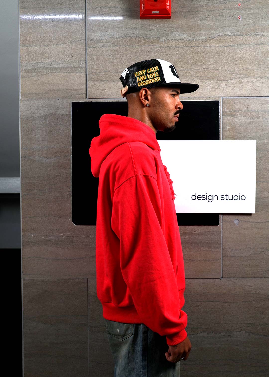 Man in red hoodie near design studio sign.