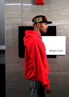 Man in red hoodie and cap near design studio sign.