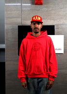 Man in red hoodie and cap standing indoors.