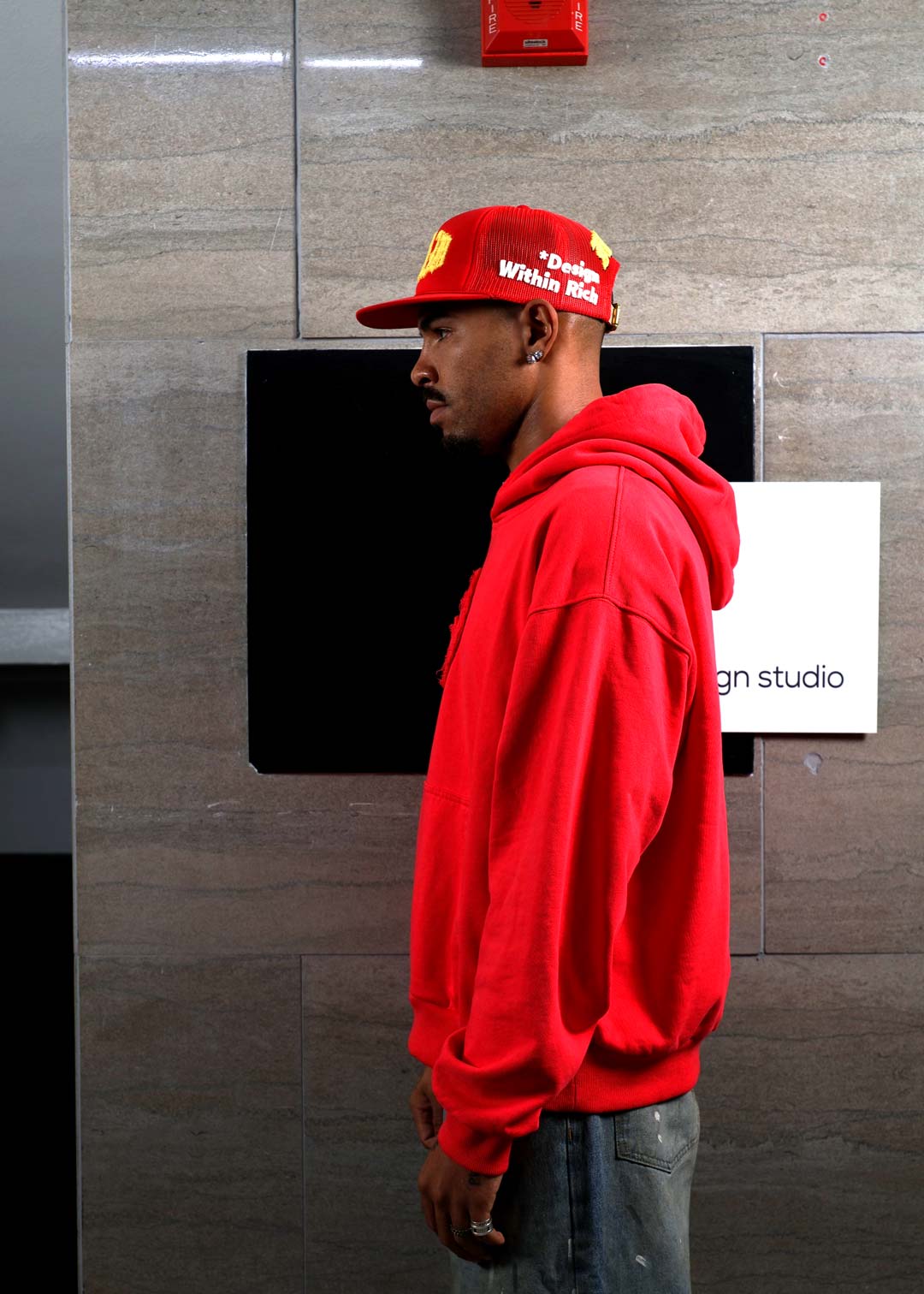 Man in red hoodie and cap, side profile.