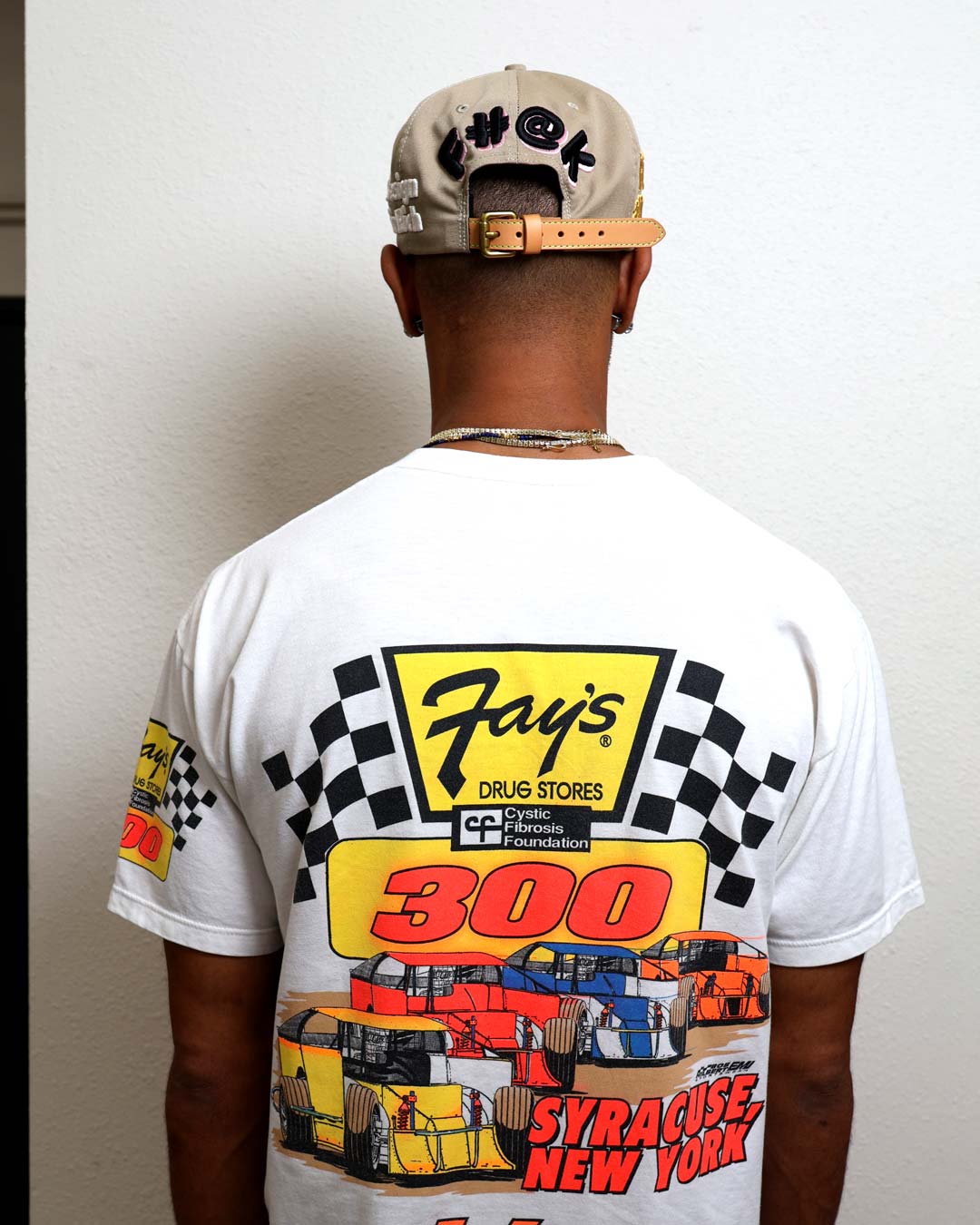 Man wearing racing-themed shirt and cap, back view.