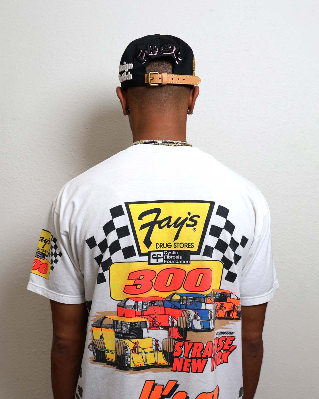 Man wearing graphic racing-themed shirt and cap.
