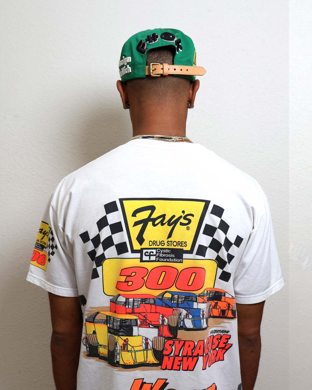 Man wearing racing-themed shirt and green cap.