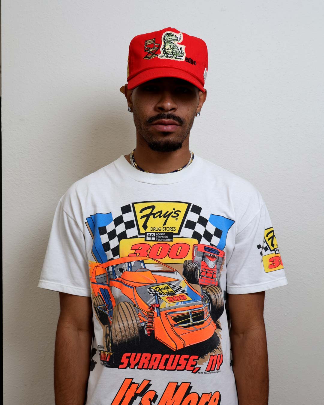 Man wearing racing-themed shirt and red cap.
