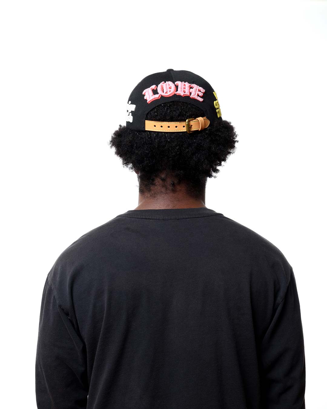 Person wearing a black cap with colorful text and a black shirt on a white background
