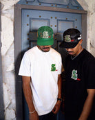 Man in cap and graphic t-shirt, standing sideways.